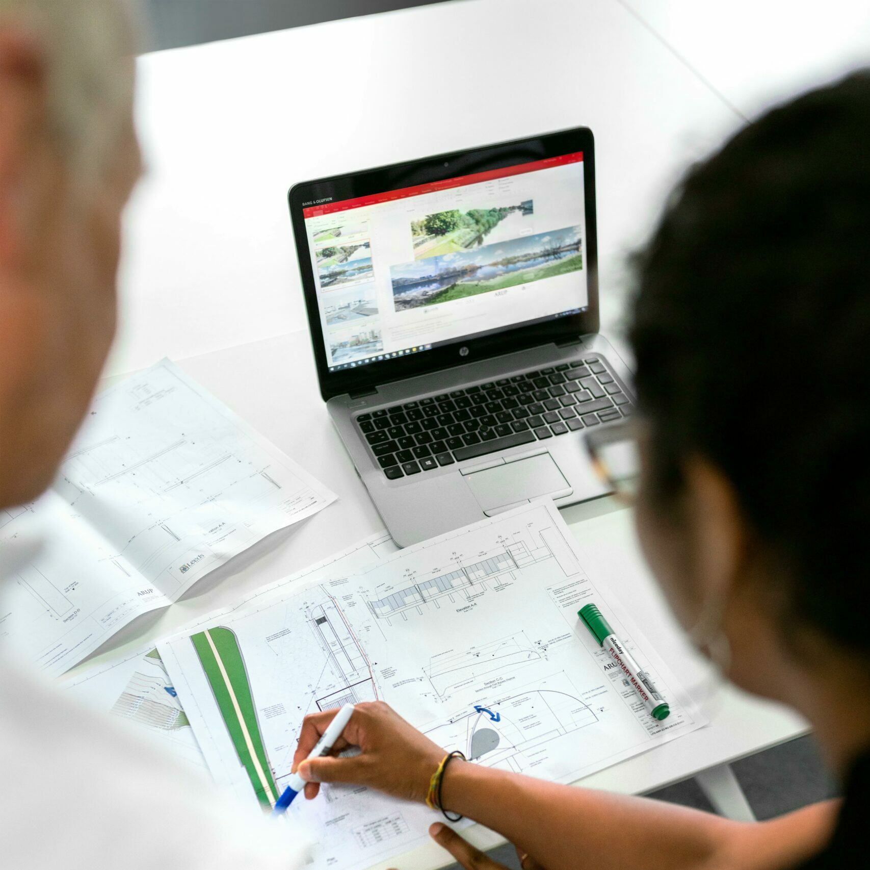 Engineers collaborate on designs with blueprints and laptops in a modern office setting.